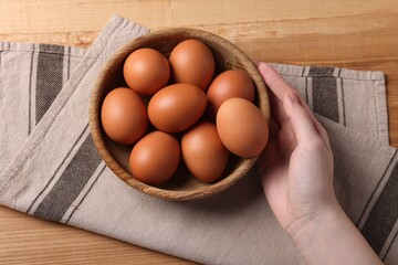 Woman with raw eggs at wooden table, top view