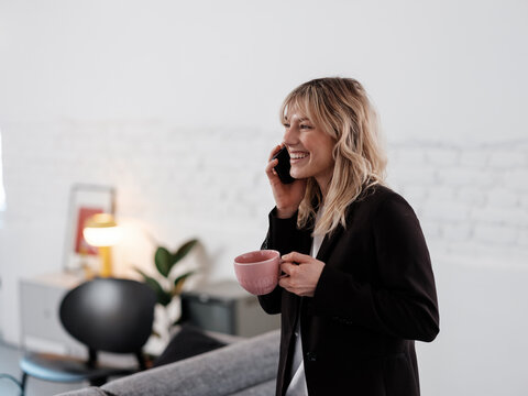 Smiling Professional Woman Holding Coffee Mug While Talking On Phone 