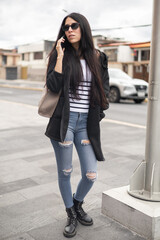Obraz premium Lovely girl talking on her cellphone in the city, exuding a relaxed and confident vibe while navigating the urban surroundings.