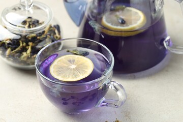 Delicious butterfly pea flower tea with lemon on gray textured table, closeup
