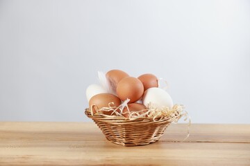 Many raw eggs in basket on wooden table. Space for text