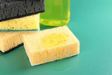 Sponge with detergent and stack of ones on green background, closeup
