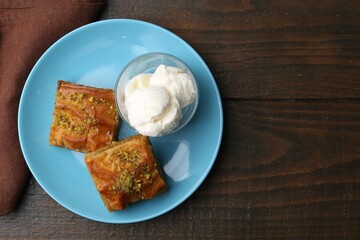 Tasty baklava with chopped nuts and scoops of ice cream on wooden table, top view. Space for text