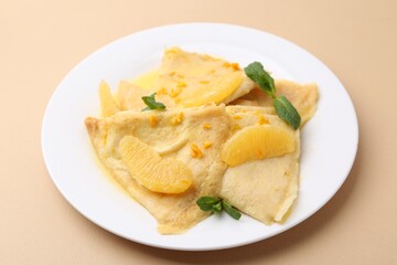 Plate with tasty crepes Suzette on beige table, closeup