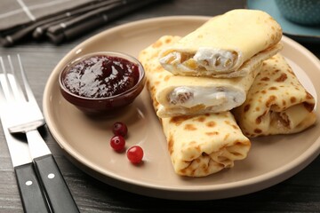 Delicious rolled crepes with cottage cheese, raisins, jam and cranberries on wooden table, closeup