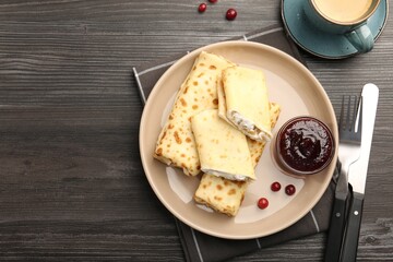 Delicious rolled crepes with cottage cheese, raisins, jam, cranberries and coffee on wooden table, flat lay. Space for text