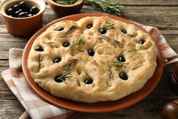 Delicious focaccia bread with olives and rosemary on wooden table, closeup