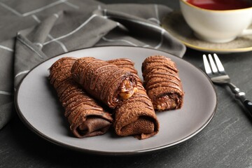 Delicious chocolate crepes with sweet paste and nuts on black table, closeup