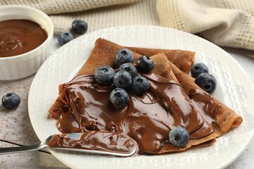Delicious chocolate crepes with sweet paste and blueberries on table, closeup