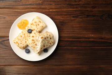 Delicious crepes with cottage cheese, jam and blueberries on wooden table, top view. Space for text