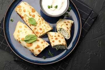 Delicious crepes with cottage cheese, spinach and sour cream on black table, top view