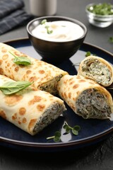 Delicious crepes with cottage cheese, spinach and sour cream on black table, closeup