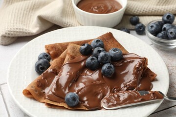 Delicious chocolate crepes with sweet paste and blueberries on table, closeup