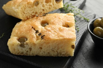 Pieces of delicious focaccia bread with olives and thyme on black table, closeup