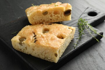 Pieces of delicious focaccia bread with olives and thyme on black table, closeup