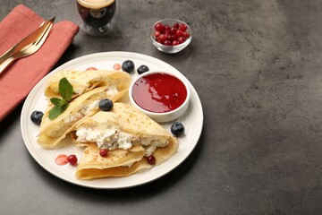 Delicious crepes with cottage cheese, jam, redcurrants and blueberries served on grey table. Space for text