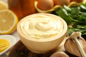 Delicious mayonnaise sauce in bowl and garlic on table, closeup