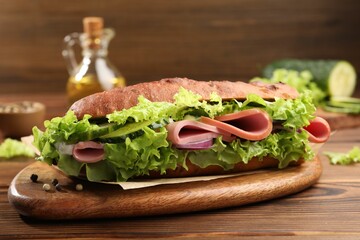 Delicious baguette sandwich with ham on wooden table, closeup