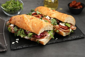Halves of baguette sandwich with prosciutto and sun dried tomatoes on grey table