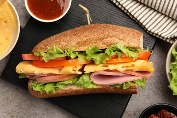 Delicious baguette sandwich with ham and ingredients on grey table, flat lay