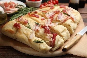 Slices of delicious focaccia bread with bacon, rosemary and knife on wooden table, closeup