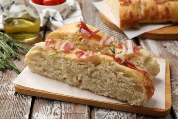 Slices of delicious focaccia bread with bacon and rosemary on wooden table, closeup