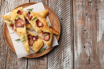 Slices of delicious focaccia bread with bacon and rosemary on wooden table, top view. Space for text