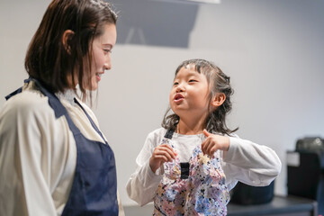 A Japanese parent and child, a woman in her 30s, a man in his 20s, and a 6-year-old girl, are making Japanese pickles by packing cut cucumbers into a bag in their home kitchen.