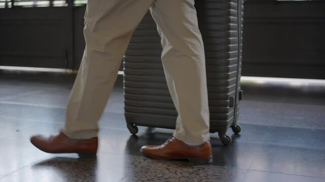 In a modern train station, a stylish traveler confidently walks on polished floors with a sleek silver suitcase, dressed in cream pants and elegant brown shoes, embodying sophistication and comfort
