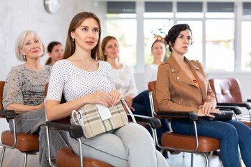 Young smiling woman in casual clothes listening to speaker lecture while sitting in office