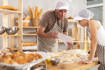 Thoughtful male baker and teenage girl are looking at paper while baking in bakehouse