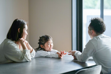A Japanese parent and child, a woman in her 30s, a man in his 20s, and a 6-year-old girl, are playing with their hands at a table in their living room.