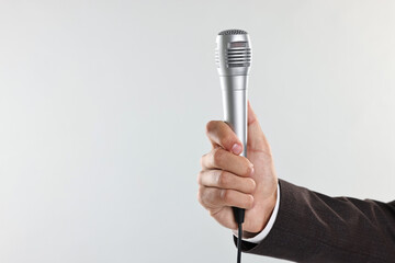 Man with microphone on light grey background, closeup. Space for text