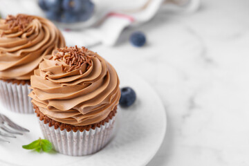 Tasty cupcakes with chocolate cream and blueberries on white marble table, closeup. Space for text