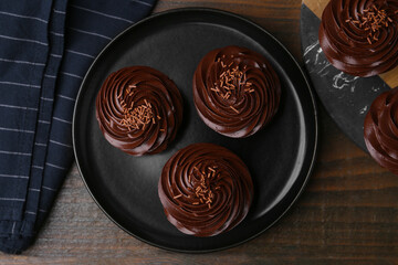 Tasty cupcakes with chocolate cream on wooden table, top view