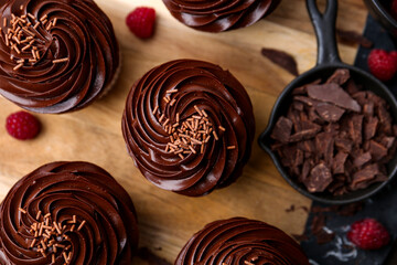 Tasty cupcakes with chocolate cream and raspberries on wooden table, flat lay