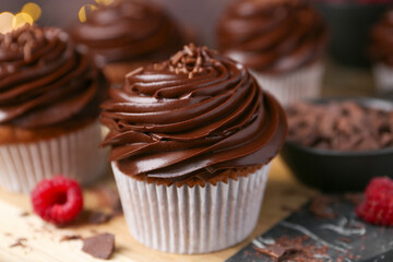 Tasty cupcakes with chocolate cream and raspberries on wooden table, closeup