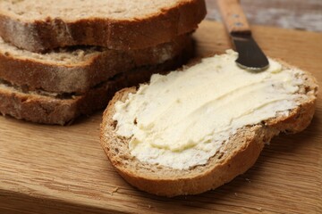 Fresh bread with butter and knife on wooden board, closeup