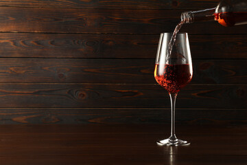 Pouring rose wine into glass at wooden table, space for text