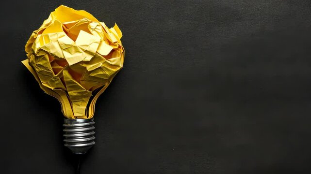 Bright idea represented by a crumpled yellow paper light bulb on a black background