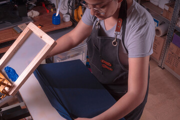 Young white-skinned Latina woman doing printing work using the screen printing and printing with meshes method. It could be for industry or sales. Advertising uses different tools or objects. She is h