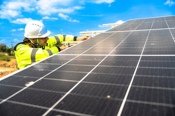 A solar technician in a high-visibility jacket and helmet stands next to a solar panel, with a...
