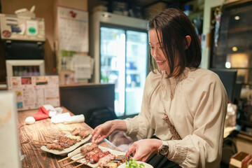 A Japanese female parent and child in their 30s are watching yakitori dishes at an izakaya.
