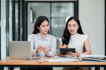 Obraz premium Two businesswomen working together in a contemporary office setting, using digital tablets and laptops for collaboration.