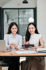 Two businesswomen working together in a contemporary office, using digital tablets and laptops for collaboration.