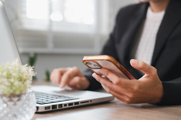 Professional working on a laptop while checking a smartphone in a bright, modern office environment.