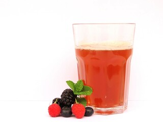 Raspberries, blackberries, blueberries and mint leaves beside a glass of cold red fruit tea with white background. 