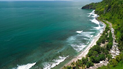 Aerial drone view of coastline with hills and trees, as well as view of coral cliffs and sea with waves from the ocean in Menganti Beach Kebumen Central Java Indonesia