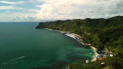 Aerial drone view of coastline with hills and trees, as well as view of coral cliffs and sea with waves from the ocean in Menganti Beach Kebumen Central Java Indonesia