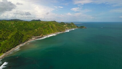 Fototapeta premium Aerial drone view of coastline with hills and trees, as well as view of coral cliffs and sea with waves from the ocean in Menganti Beach Kebumen Central Java Indonesia